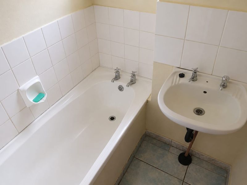 A functional bathroom featuring a standard bathtub and pedestal basin with white wall tiling and tiled flooring.