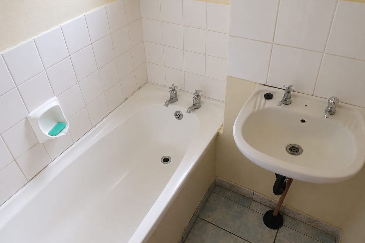 A functional bathroom featuring a standard bathtub and pedestal basin with white wall tiling and tiled flooring.