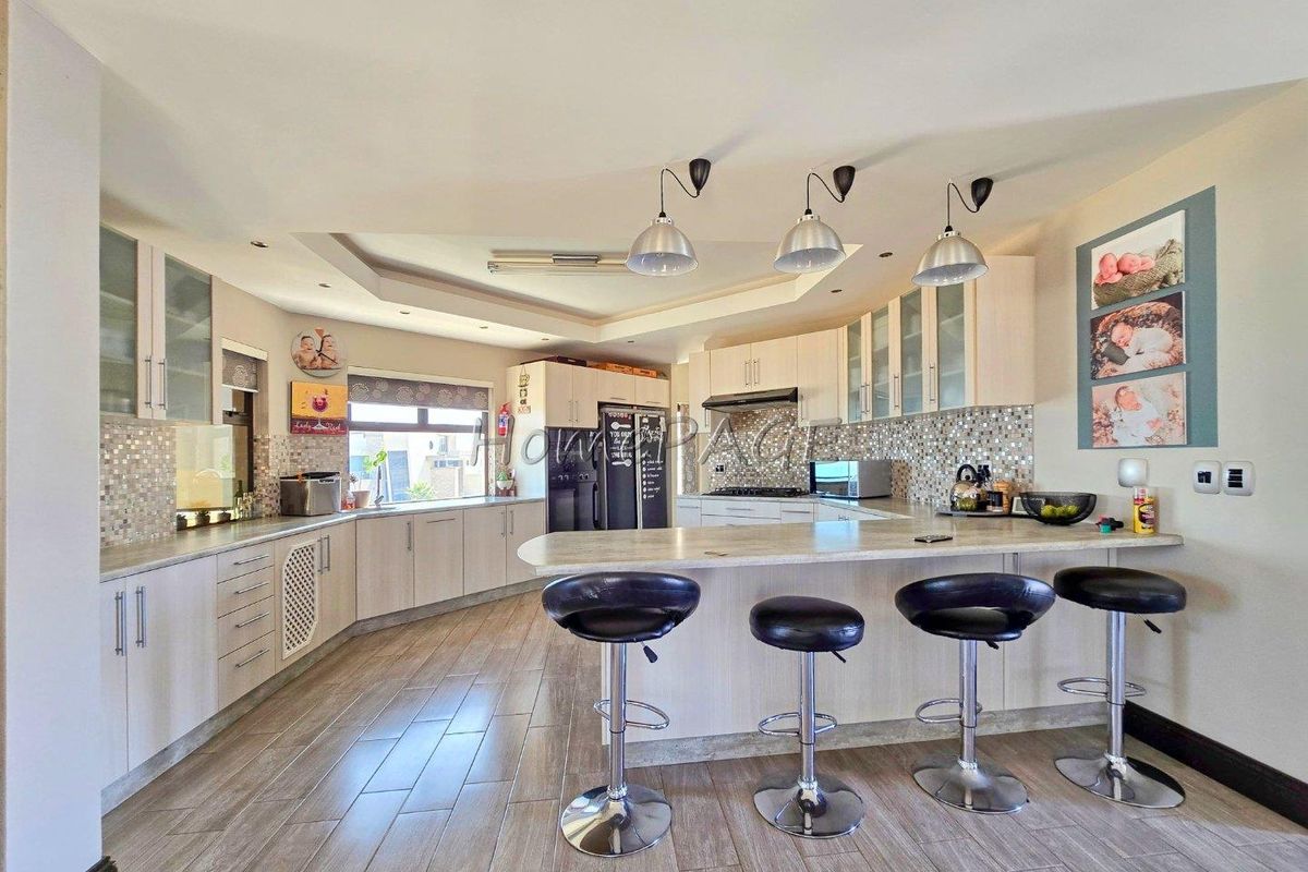 Spacious kitchen featuring light-toned cabinetry, mosaic tile backsplash, breakfast bar, and integrated lighting, offering a functional and modern culinary space.