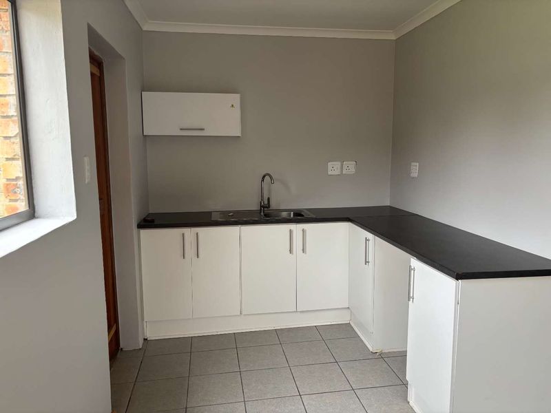 A clean, functional kitchen area featuring white cabinetry, dark countertops, a stainless steel sink, and neutral tiled flooring.