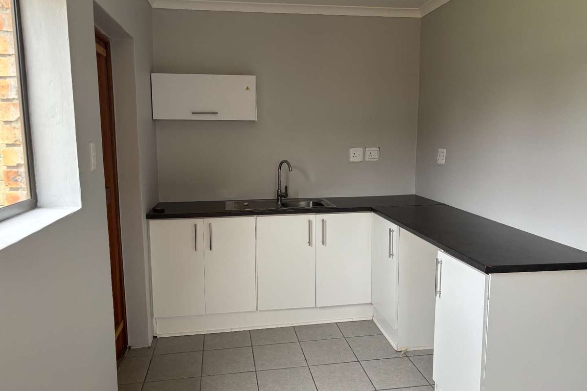 A clean, functional kitchen area featuring white cabinetry, dark countertops, a stainless steel sink, and neutral tiled flooring.
