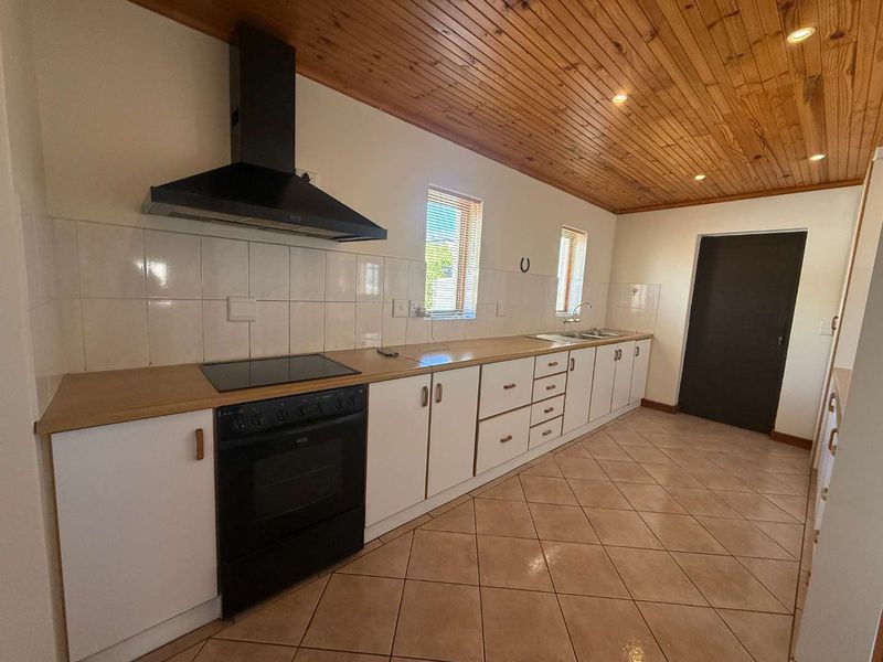 A functional kitchen featuring white cabinetry, wood-look countertops, a black oven and hob, tiled flooring, and a distinctive timber-paneled ceiling.