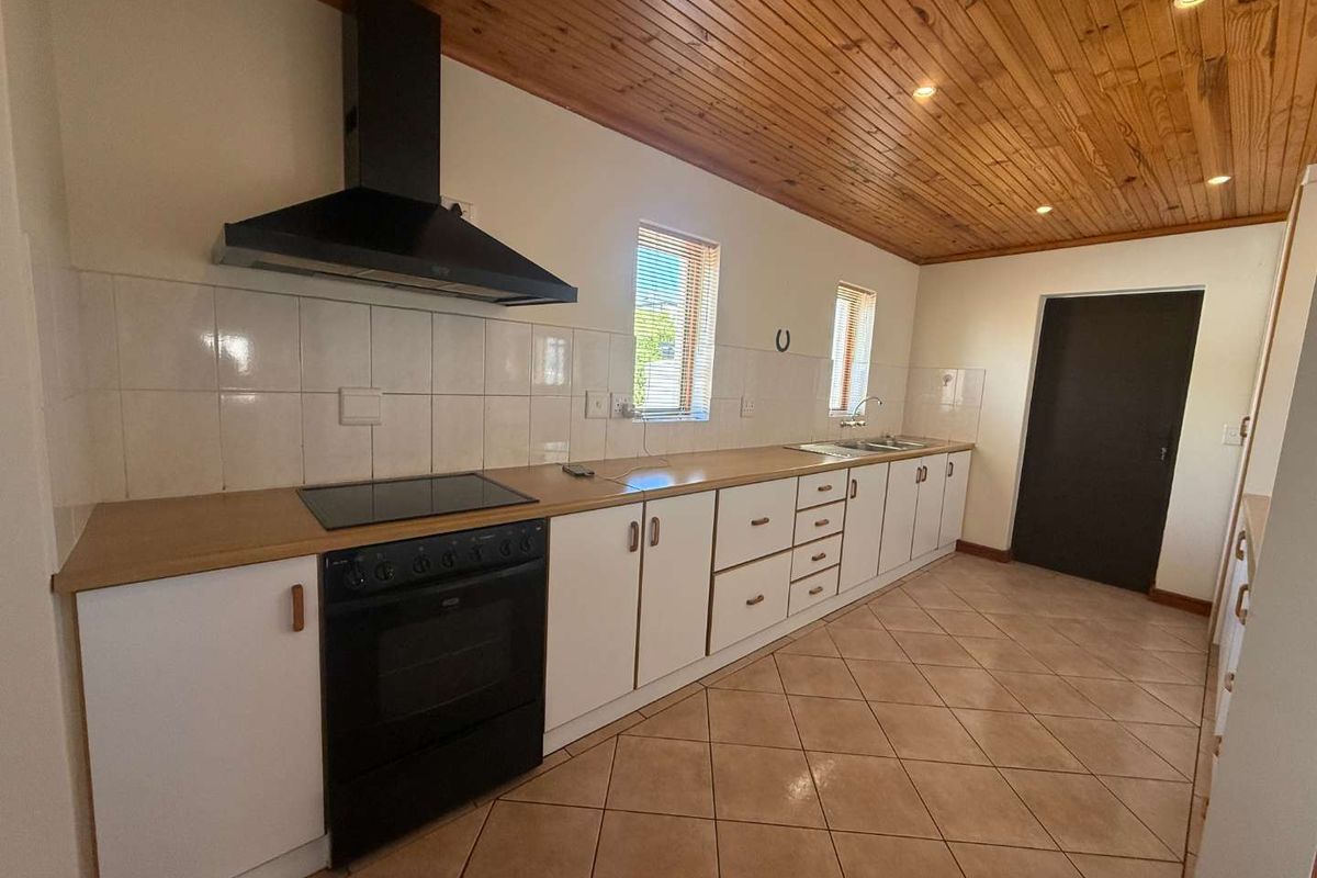 A functional kitchen featuring white cabinetry, wood-look countertops, a black oven and hob, tiled flooring, and a distinctive timber-paneled ceiling.