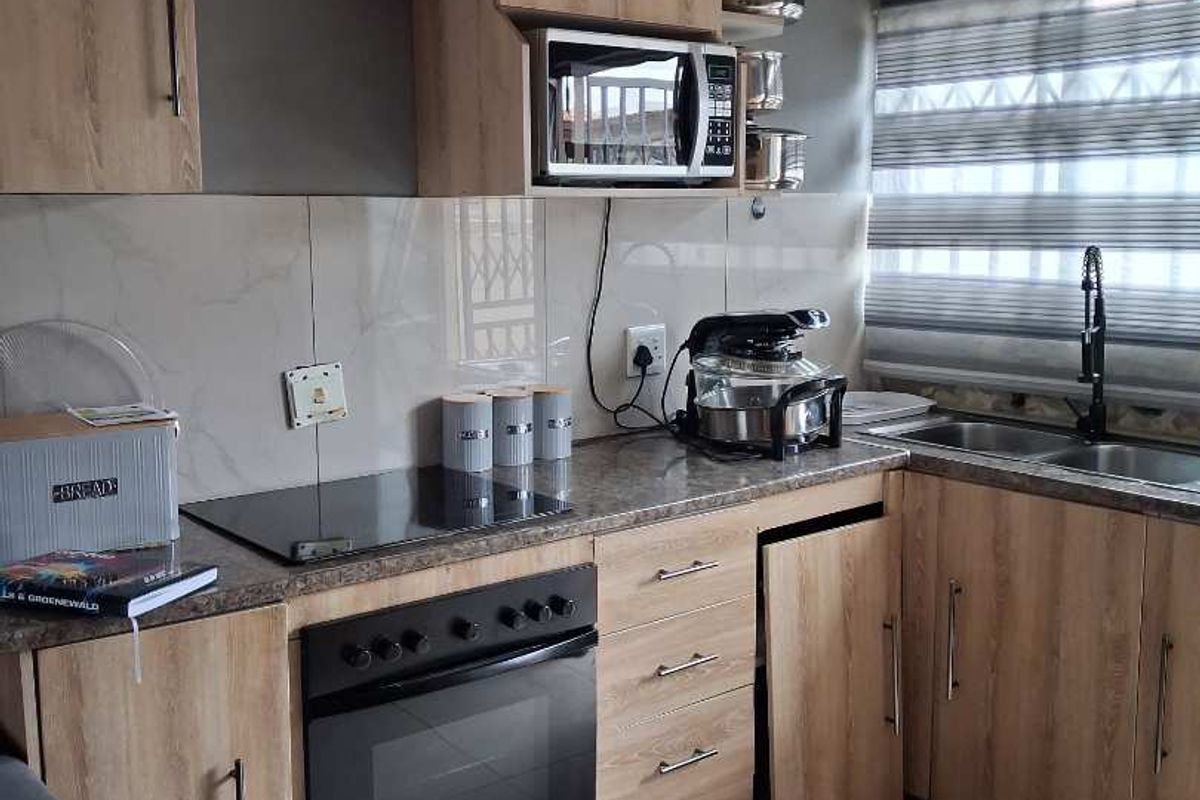 Modern kitchen featuring light wood-grain cabinetry, stone-look countertops, built-in oven, induction hob, and tiled flooring with a double sink.