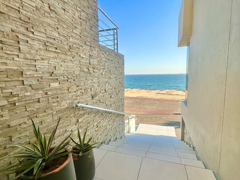 A modern exterior staircase featuring stone cladding and stainless steel railings, leading directly towards a scenic beach and ocean view.