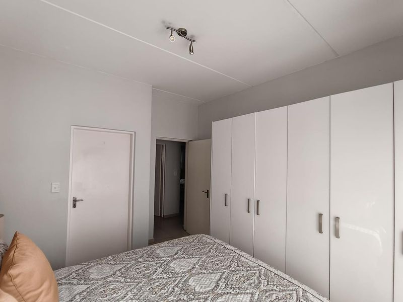 A bedroom featuring white built-in cupboards with modern handles and a ceiling-mounted spotlight fixture.