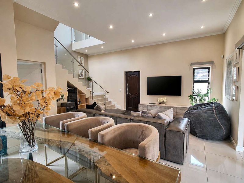Spacious open-plan living area featuring modern tiled floors, recessed lighting, and a contemporary staircase with a glass balustrade leading to the upper level.