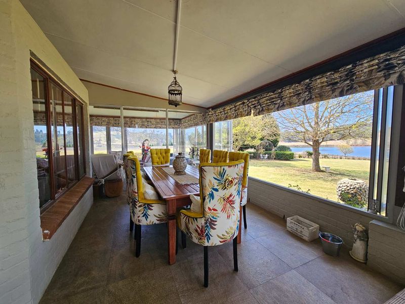 A spacious enclosed patio featuring tiled flooring, large windows with scenic garden and lake views, and a bright, airy atmosphere.