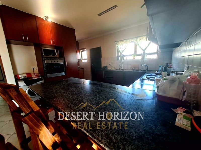 A functional kitchen featuring dark wood cabinetry, granite countertops, built-in oven, and hob, with tiled flooring and natural light from the window.