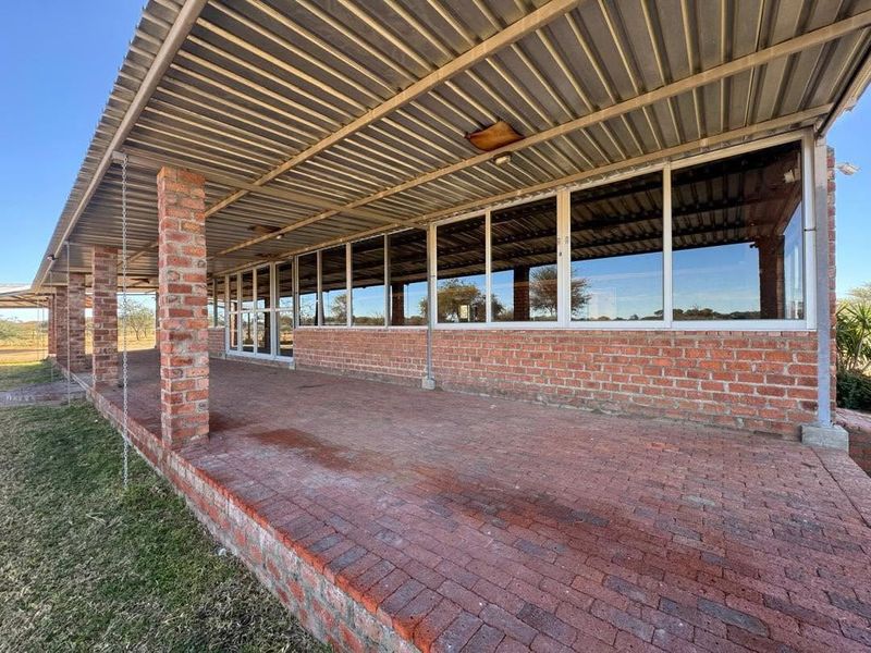 Spacious covered patio featuring exposed brick pillars, brick paving, and extensive aluminium-framed glazing, offering a functional outdoor entertainment area.