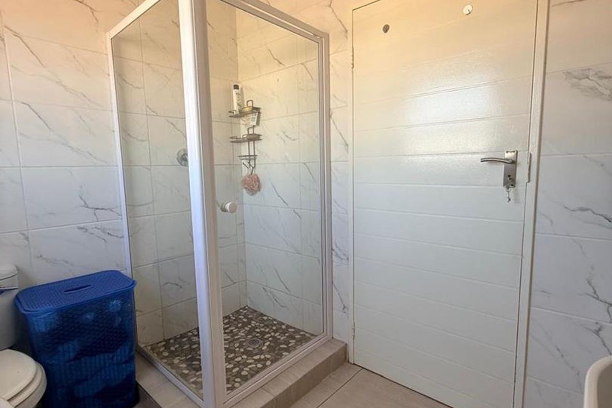 A bathroom featuring marble-look wall tiles, a raised shower enclosure with a pebble-style floor, and a standard white interior door.