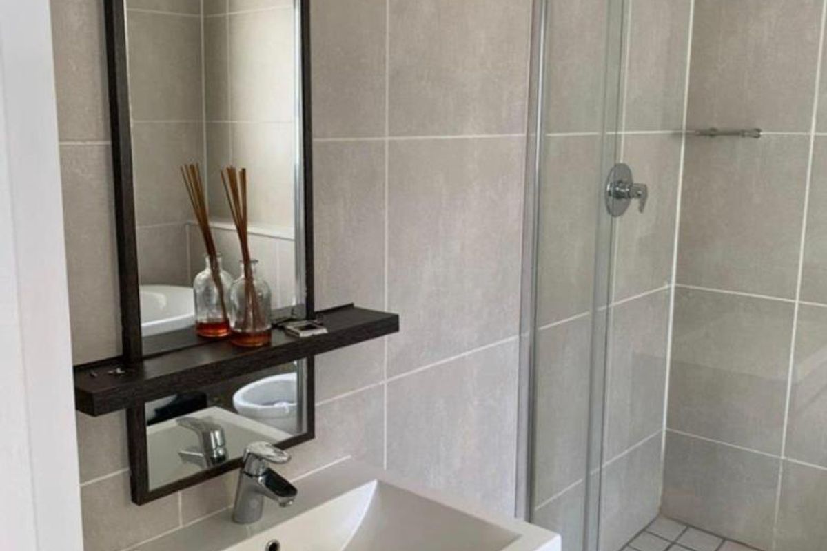 A modern bathroom featuring a vanity cabinet with a basin, a wall-mounted mirror, and a glass-enclosed shower with neutral wall tiling.