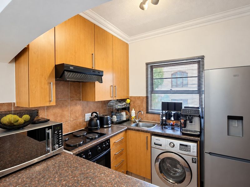 Compact kitchen featuring wood-finish cabinetry, granite-look countertops, tiled backsplash, built-in hob with extractor, and integrated laundry plumbing.