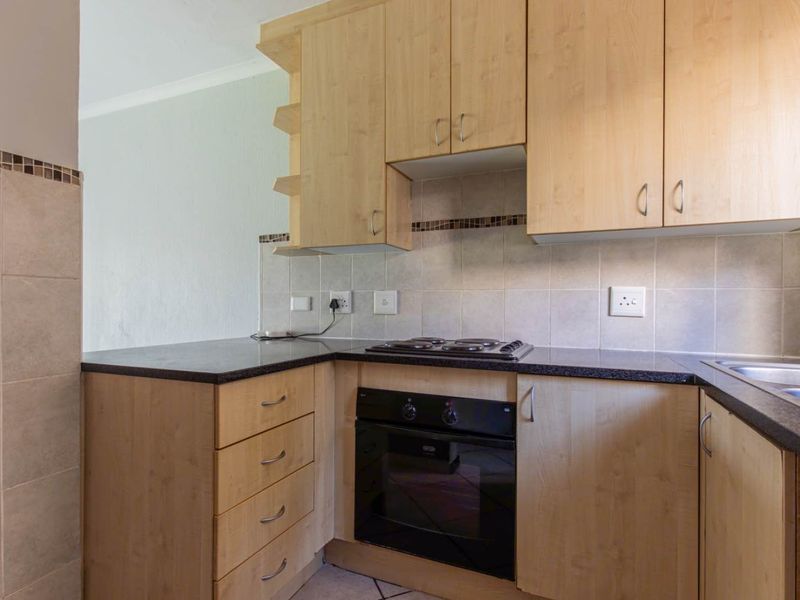 A functional kitchen featuring light wood-finish cabinetry, dark laminate countertops, a built-in oven, electric hob, and a tiled backsplash.