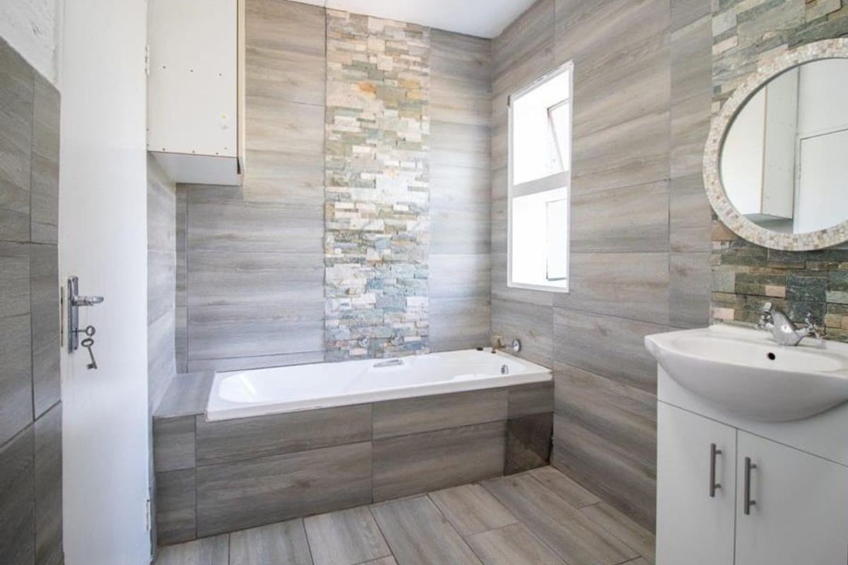 A modern bathroom featuring wood-look wall and floor tiles, a built-in bathtub with stone accent tiling, and a vanity basin.