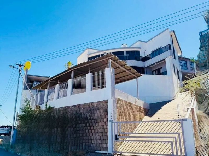 Front exterior view of a multi-level hotel property featuring a paved driveway, metal security gate, retaining wall, and covered carport area.