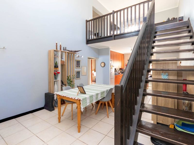 Open plan living area featuring a timber staircase leading to a mezzanine level, with tiled flooring throughout.