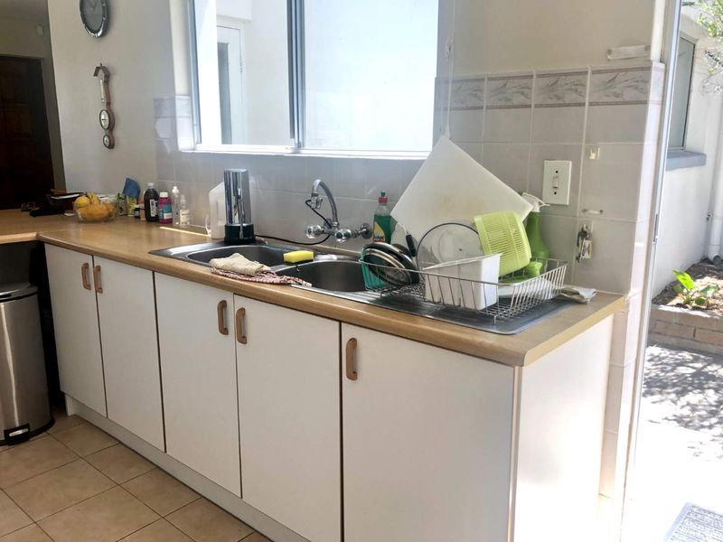 A functional kitchen area featuring a double bowl stainless steel sink, laminate countertops, and tiled backsplash with ample built-in cabinetry.