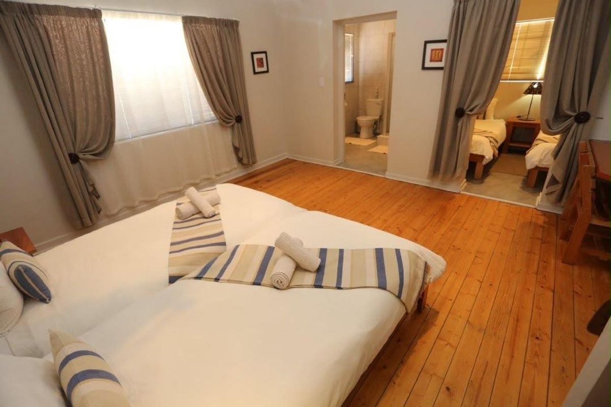 A bedroom featuring hardwood flooring, an en-suite bathroom, and natural light through window blinds.