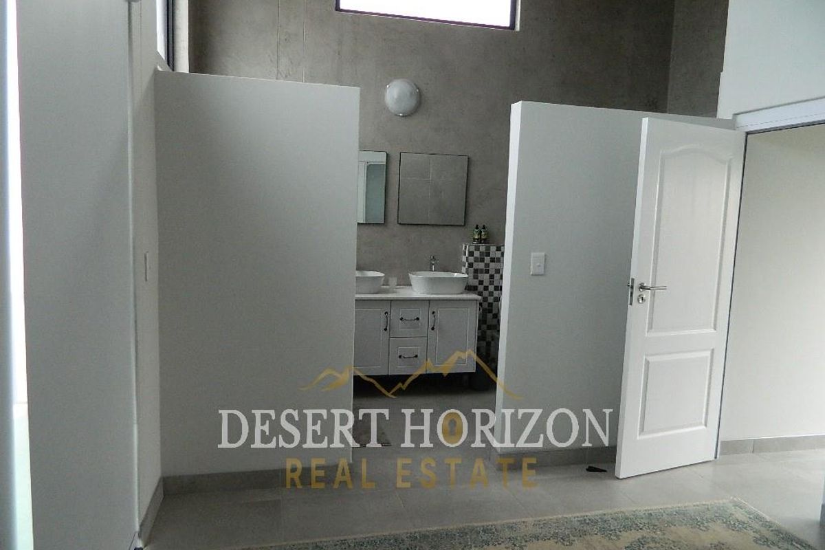 A bathroom featuring a double vanity with vessel sinks, concrete-style wall finishes, and a high-level clerestory window for natural light.