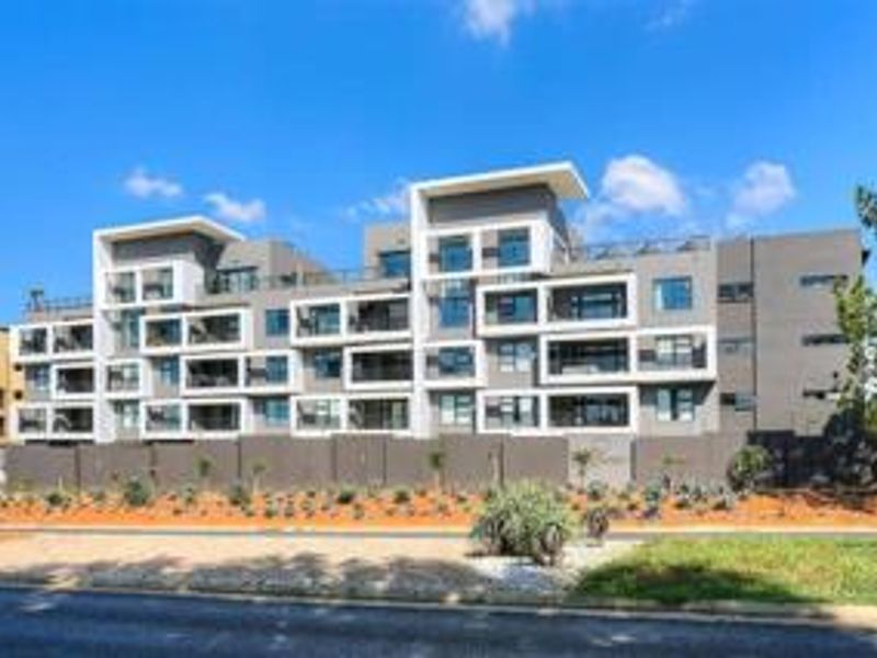 A modern multi-story apartment complex featuring contemporary architectural design, private balconies, and a secure boundary wall.