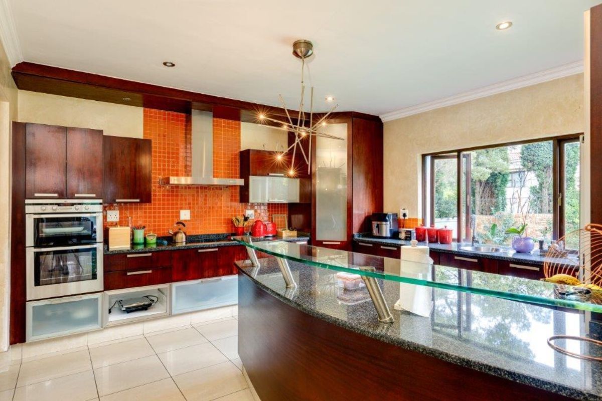 A well-appointed kitchen featuring dark wood cabinetry, granite countertops, a glass breakfast bar, and a vibrant orange mosaic tile backsplash with integrated appliances.