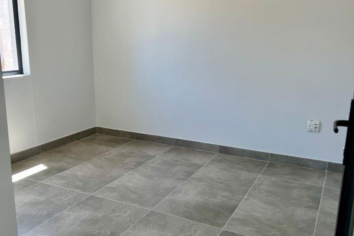 A clean, empty bedroom featuring neutral wall paint and modern grey tiled flooring with matching skirting boards.