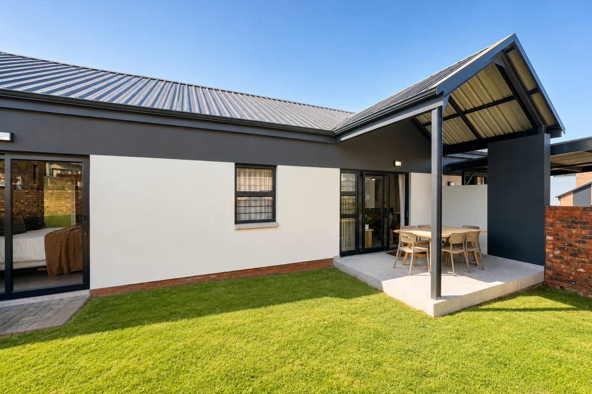 A well-maintained townhouse exterior featuring a covered patio, metal roof, and a neat, landscaped garden area.