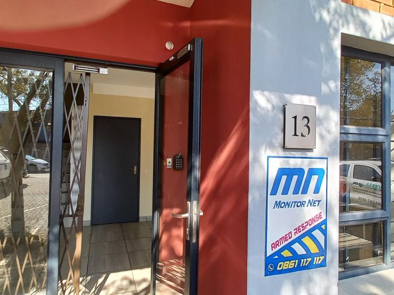 Industrial unit entrance featuring a secure glass door with security gate, brick facade, and prominent signage.