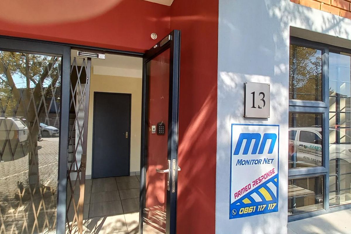 Industrial unit entrance featuring a secure glass door with security gate, brick facade, and prominent signage.
