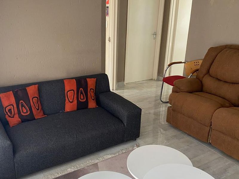 A living room area featuring tiled flooring and multiple internal doorways, showing signs of wear on the wall surfaces.