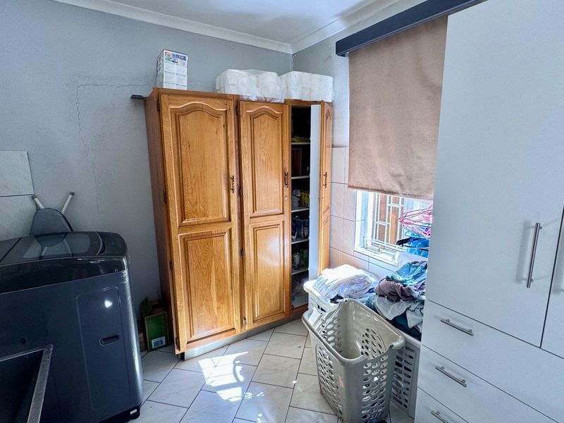 A functional laundry room featuring tiled flooring, built-in cabinetry, and a window with a roller blind.
