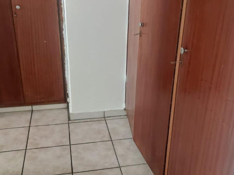 A hallway area featuring built-in wooden cupboards and tiled flooring, showing signs of wear and tear on the cabinetry and door frames.