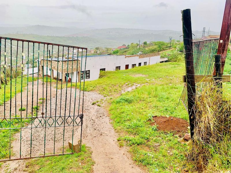 Exterior view of a property featuring a metal gate entrance, unpaved driveway, and a single-story structure with concrete block walls set in a rural landscape.