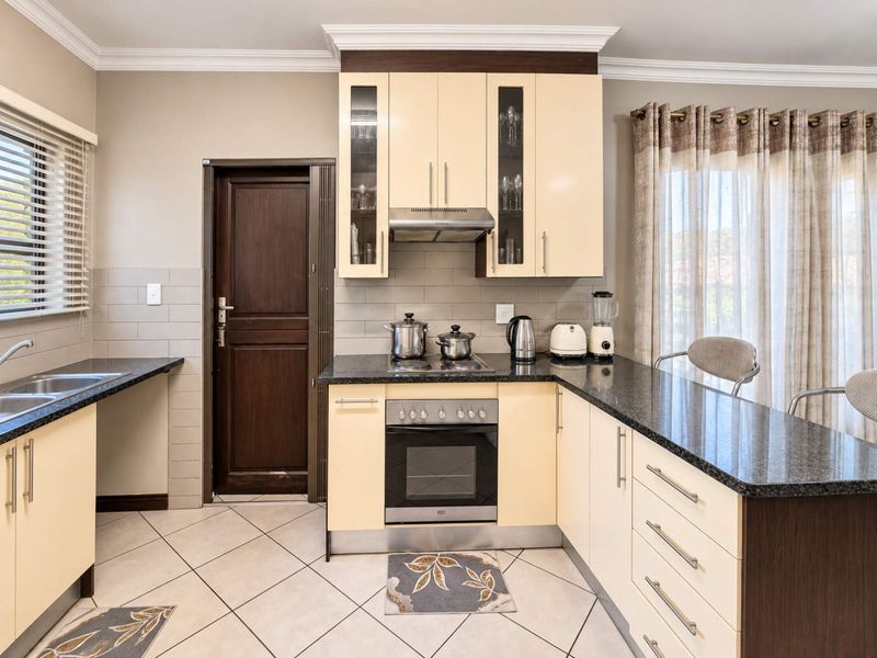 A functional kitchen featuring granite countertops, built-in oven with hob, extractor fan, and ample cabinetry, finished with tiled flooring and a neutral backsplash.