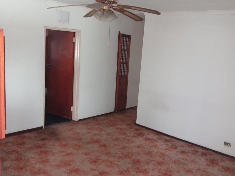 An empty living room featuring a ceiling fan and dated carpet flooring, providing a blank canvas for potential renovation and interior updates.
