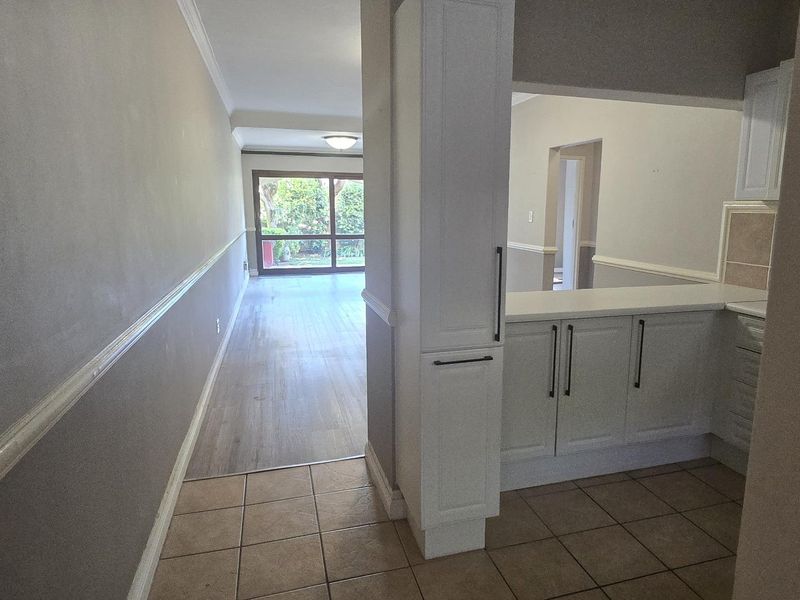 An open-plan living area featuring a kitchen with built-in cabinetry, laminate and tiled flooring, and a sliding glass door leading to the exterior.