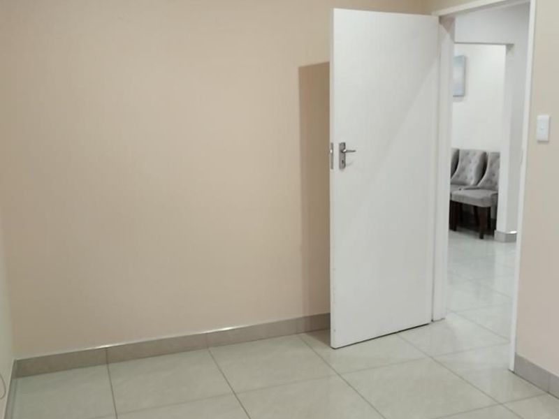 A clean, empty office space featuring neutral wall paint, tiled flooring, and a white internal door leading to an adjacent room.