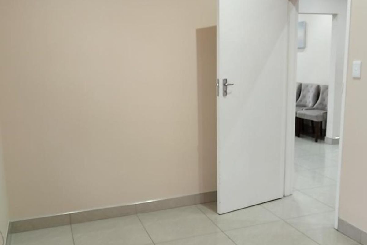 A clean, empty office space featuring neutral wall paint, tiled flooring, and a white internal door leading to an adjacent room.
