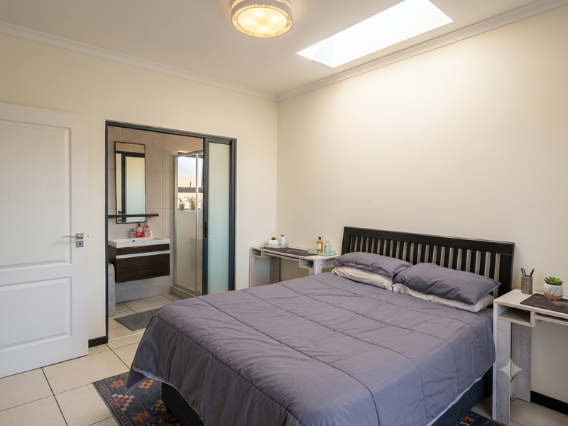 A well-lit bedroom featuring a skylight, tiled flooring, and an integrated en-suite bathroom with a modern vanity and shower enclosure.