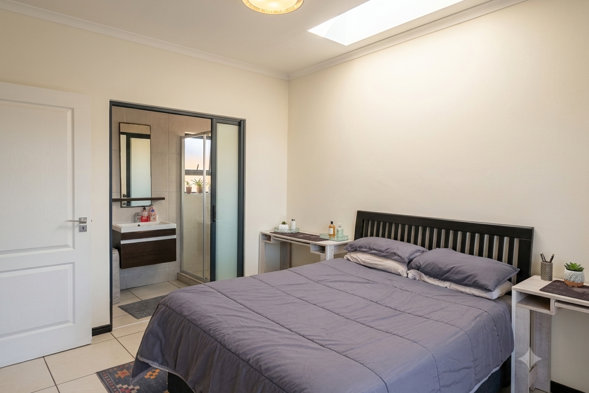 A well-lit bedroom featuring a skylight, tiled flooring, and an integrated en-suite bathroom with a modern vanity and shower enclosure.