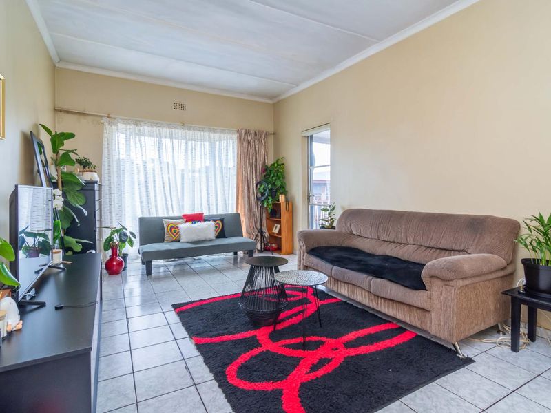 A living room featuring tiled flooring, a large window, and a sliding door, showing signs of wear on the walls and ceiling.