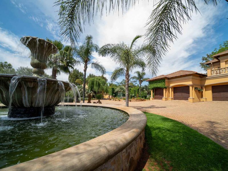 A grand front entrance featuring a large stone water fountain, a spacious paved driveway, and a triple garage with a classic tiled roof.
