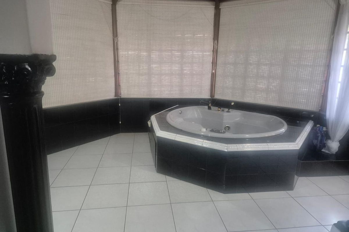 Spacious bathroom featuring a built-in corner spa bath, black tiled surround, and light-colored floor tiles under a vaulted ceiling.