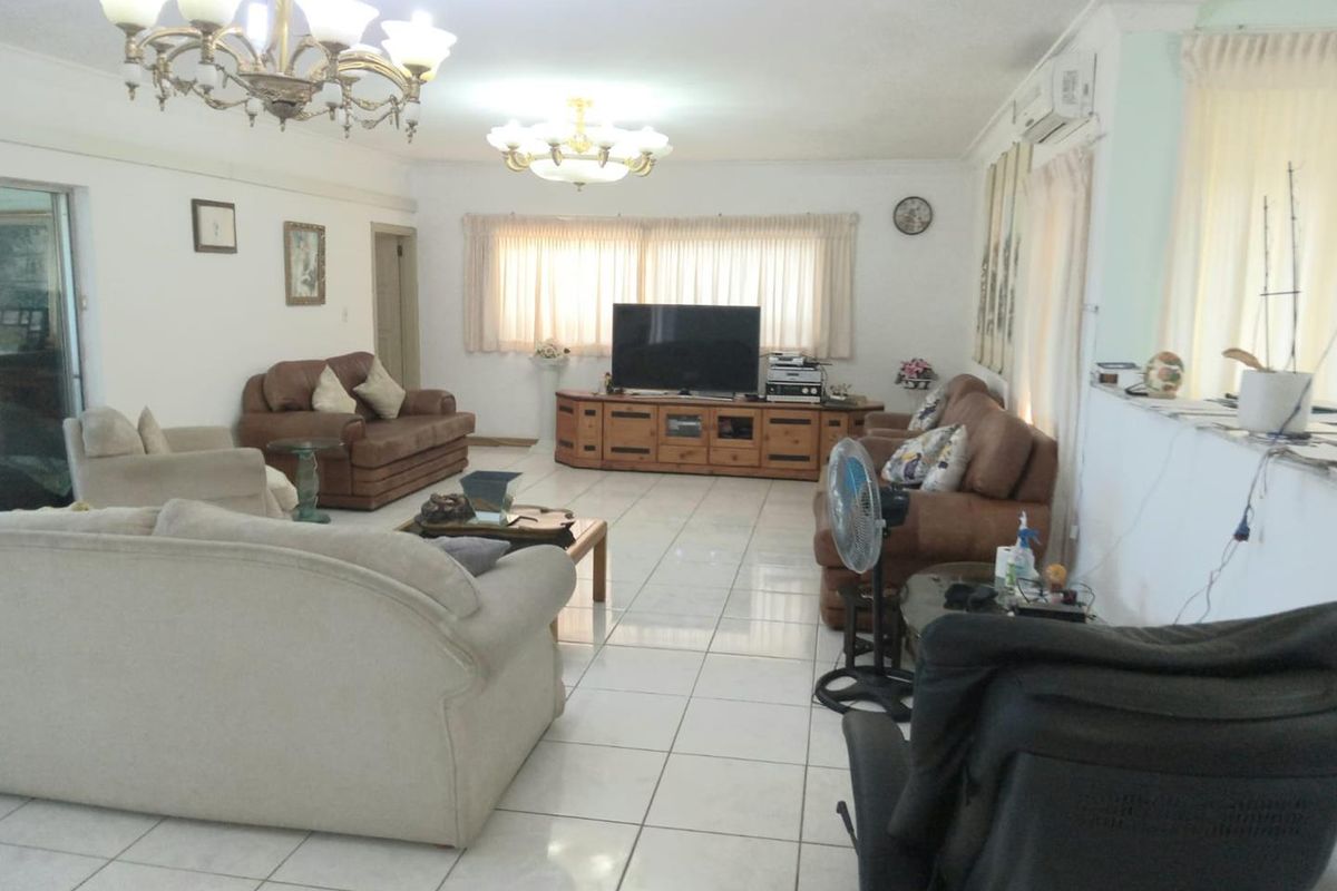 Spacious living room featuring tiled flooring, decorative chandeliers, and a wall-mounted air conditioning unit.