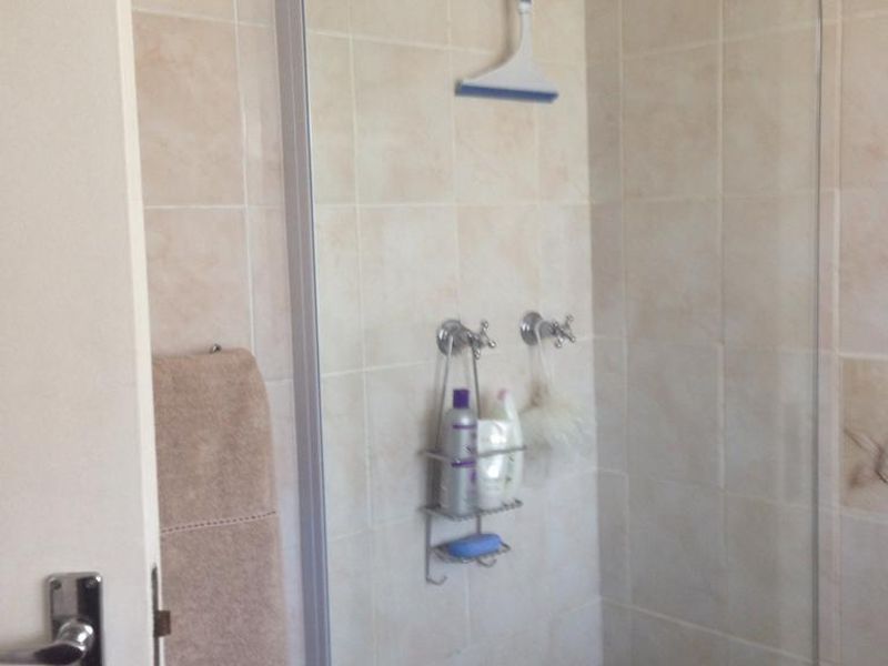 A functional bathroom featuring a bathtub with a glass shower screen and neutral wall tiling.