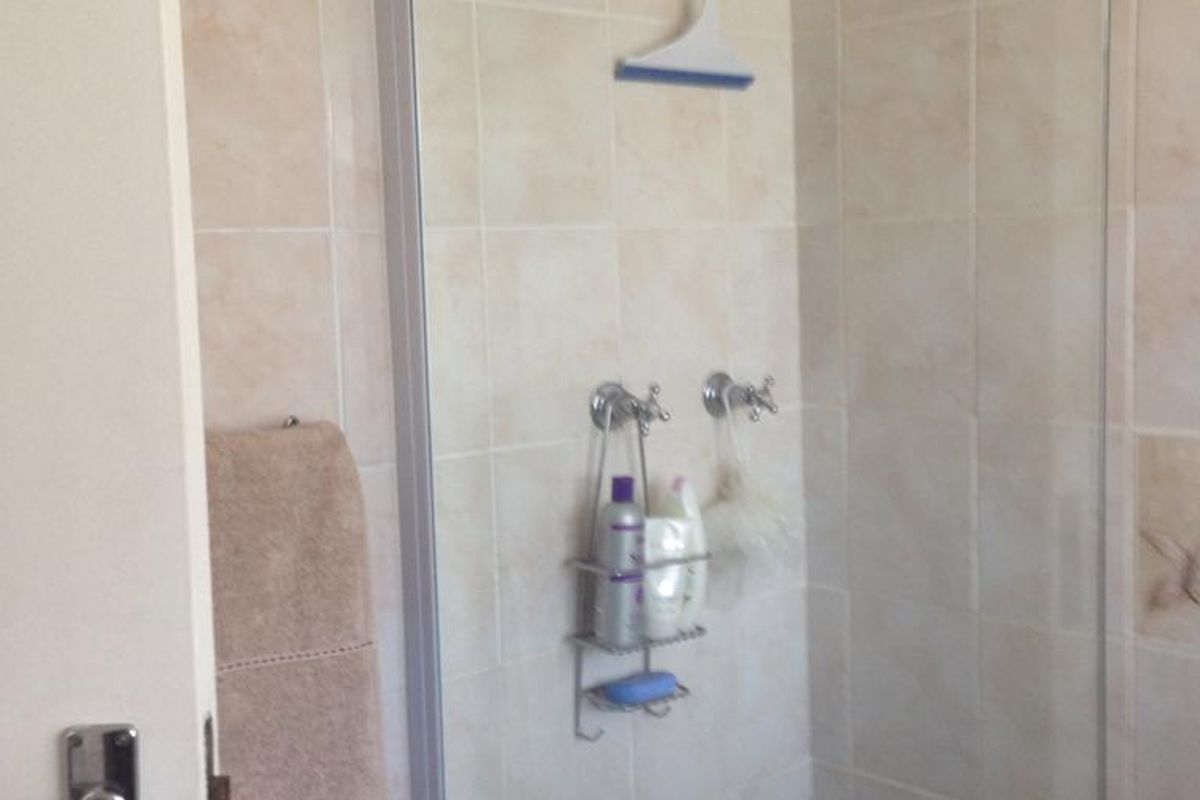 A functional bathroom featuring a bathtub with a glass shower screen and neutral wall tiling.