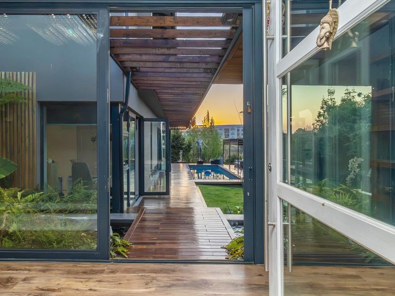 A modern covered timber deck leading to a swimming pool and landscaped garden, featuring seamless indoor-outdoor flow through large sliding glass doors.