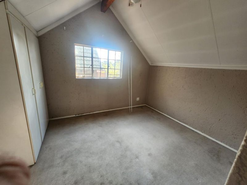 An empty bedroom featuring a pitched ceiling with an exposed beam, built-in cupboards, and a steel-framed window, offering a blank canvas for renovation.