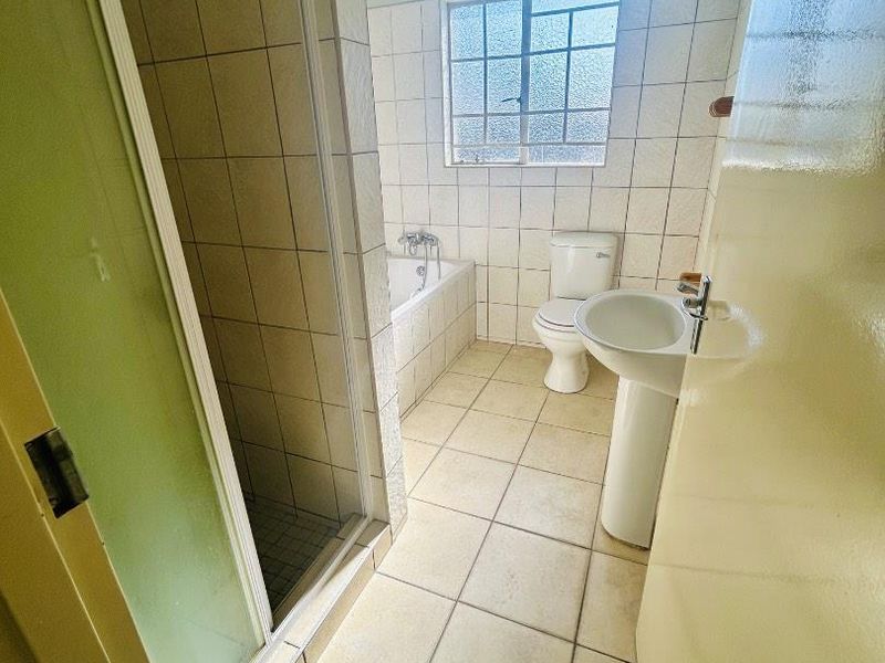 A functional bathroom featuring a separate shower enclosure, bathtub, pedestal sink, and toilet with neutral tiled finishes throughout.